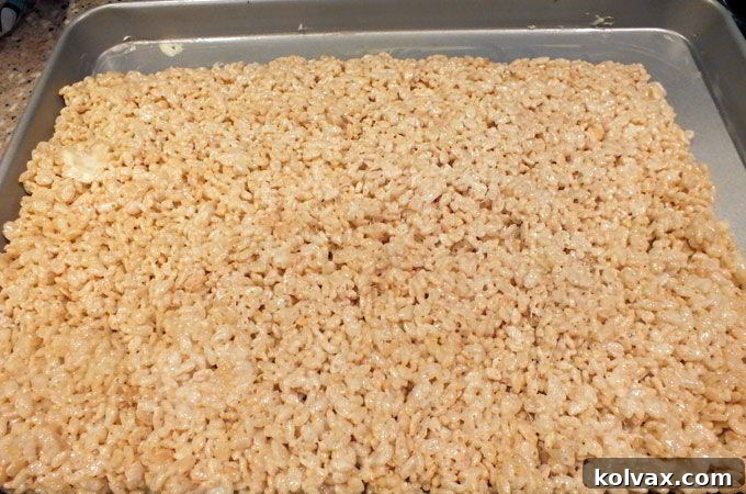 Buttered spatula pressing the Rice Krispie mixture evenly onto a cookie sheet