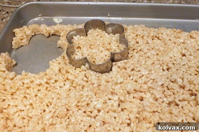 A large flower-shaped cookie cutter pressing into the cooled Rice Krispie treat mixture