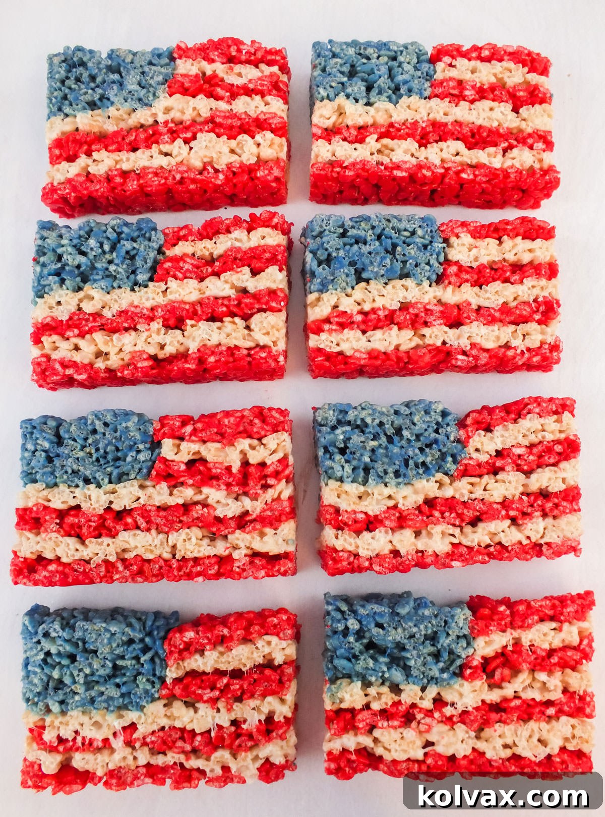 Eight perfectly cut American Flag Rice Krispie Treats arranged neatly in rows on a clean white surface, showcasing their vibrant red, white, and blue layers.