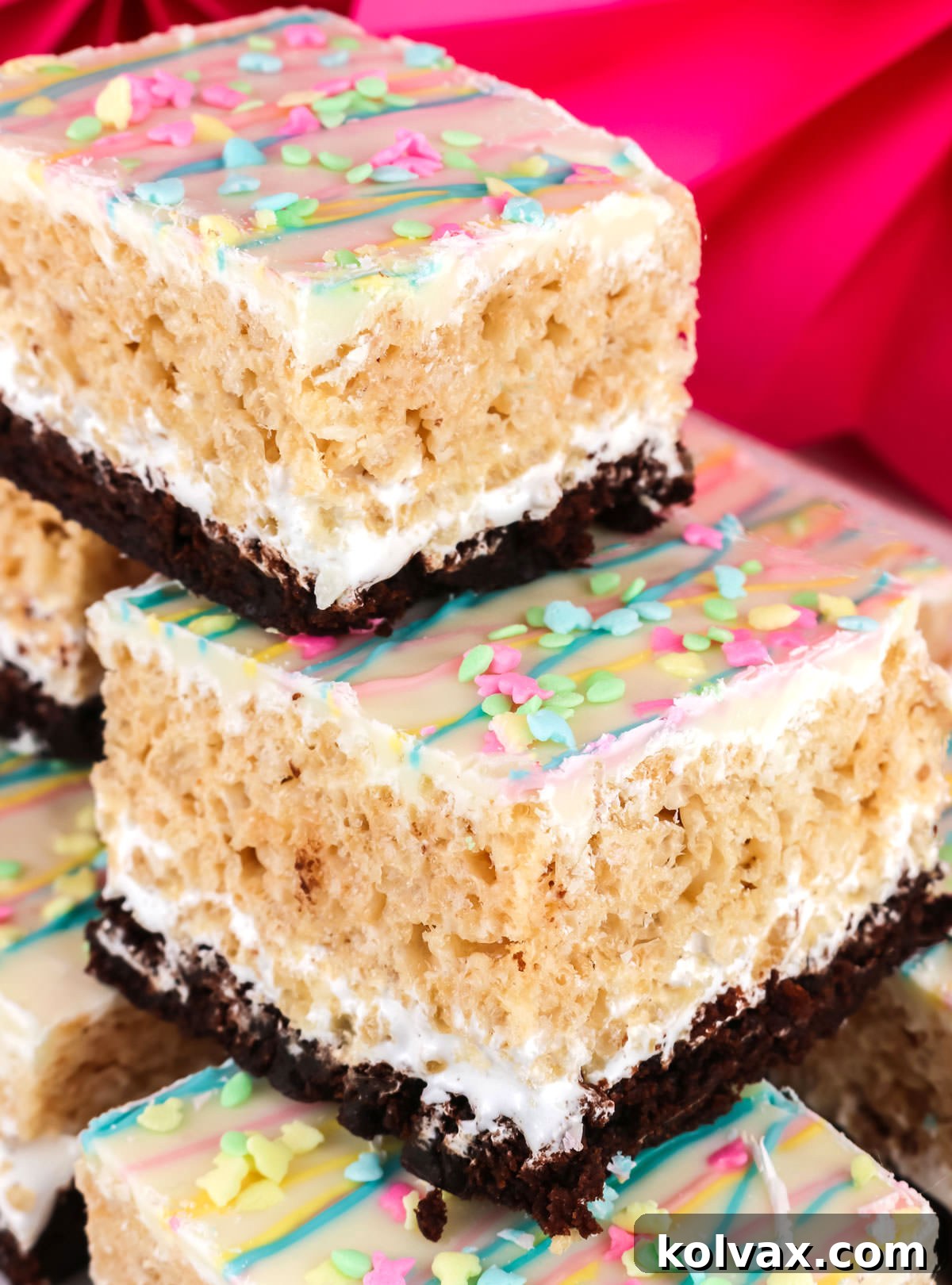 Closeup on a stack of Brownie Rice Krispie Treats in front of a pink background, highlighting the layers.