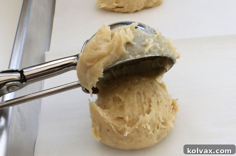 Scoops of banana cake cookie dough precisely arranged on a parchment-lined baking sheet, prepared for the oven
