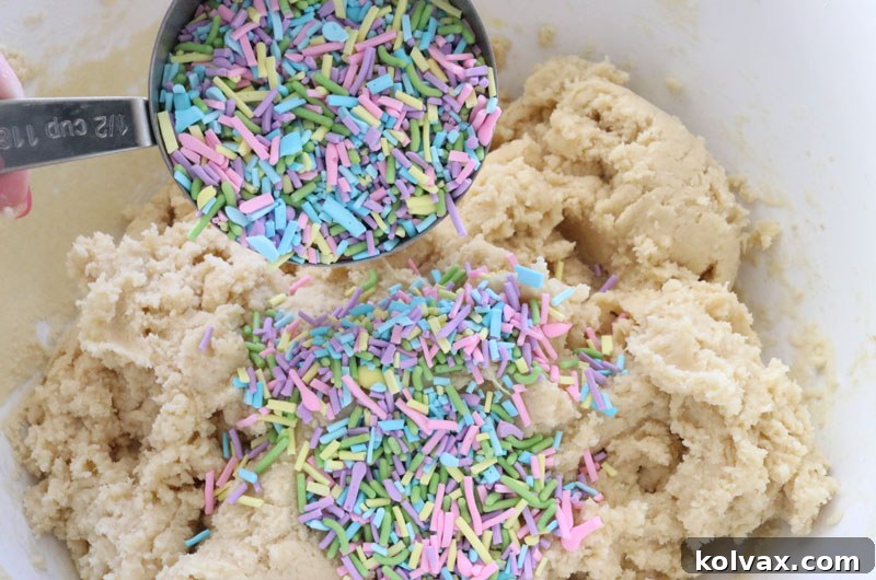 Adding colorful sprinkles to the Easter M&M Sugar Cookie Bars dough, enhancing its festive look.