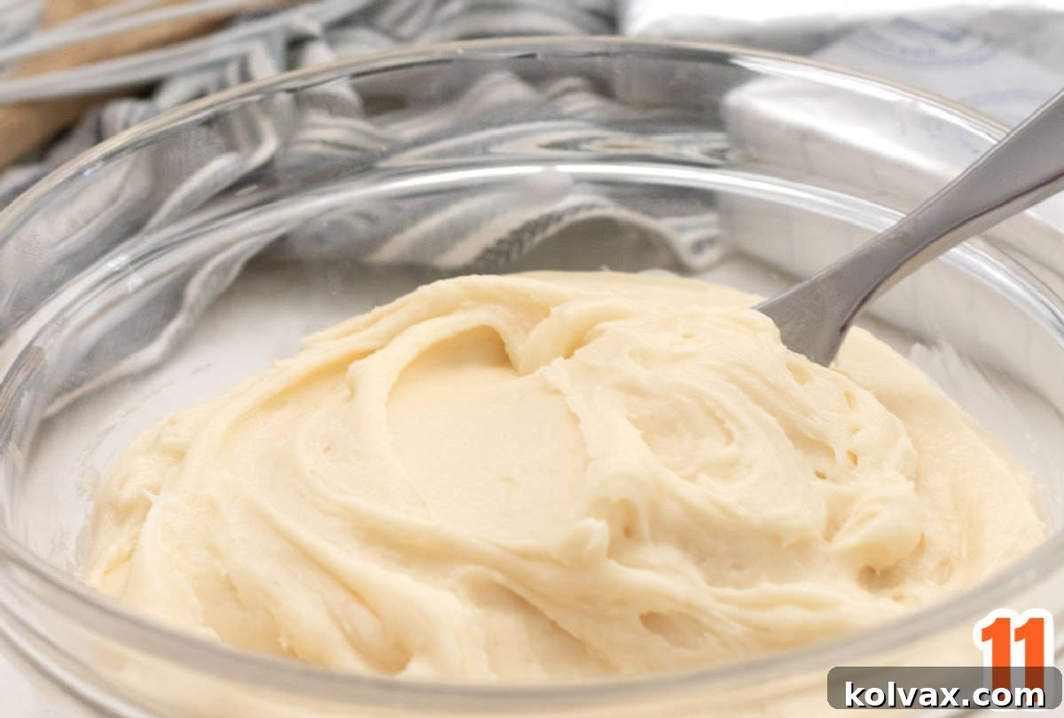 A close-up shot of a glass bowl brimming with light, fluffy, and homemade Cream Cheese Frosting, ready to adorn freshly baked cupcakes.
