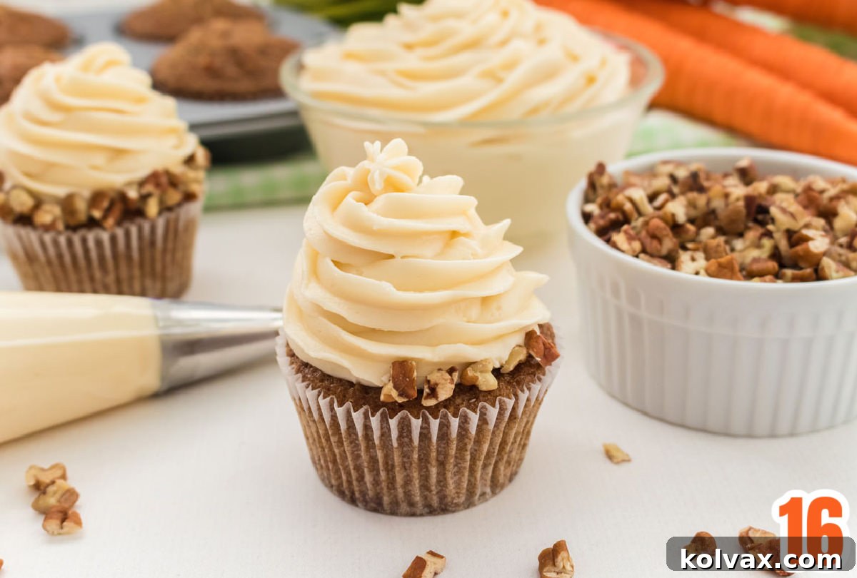 A freshly frosted Carrot Cake Cupcake with Cream Cheese Frosting, adorned with chopped nuts, next to a piping bag, a bowl of frosting, and a ramekin of nuts.