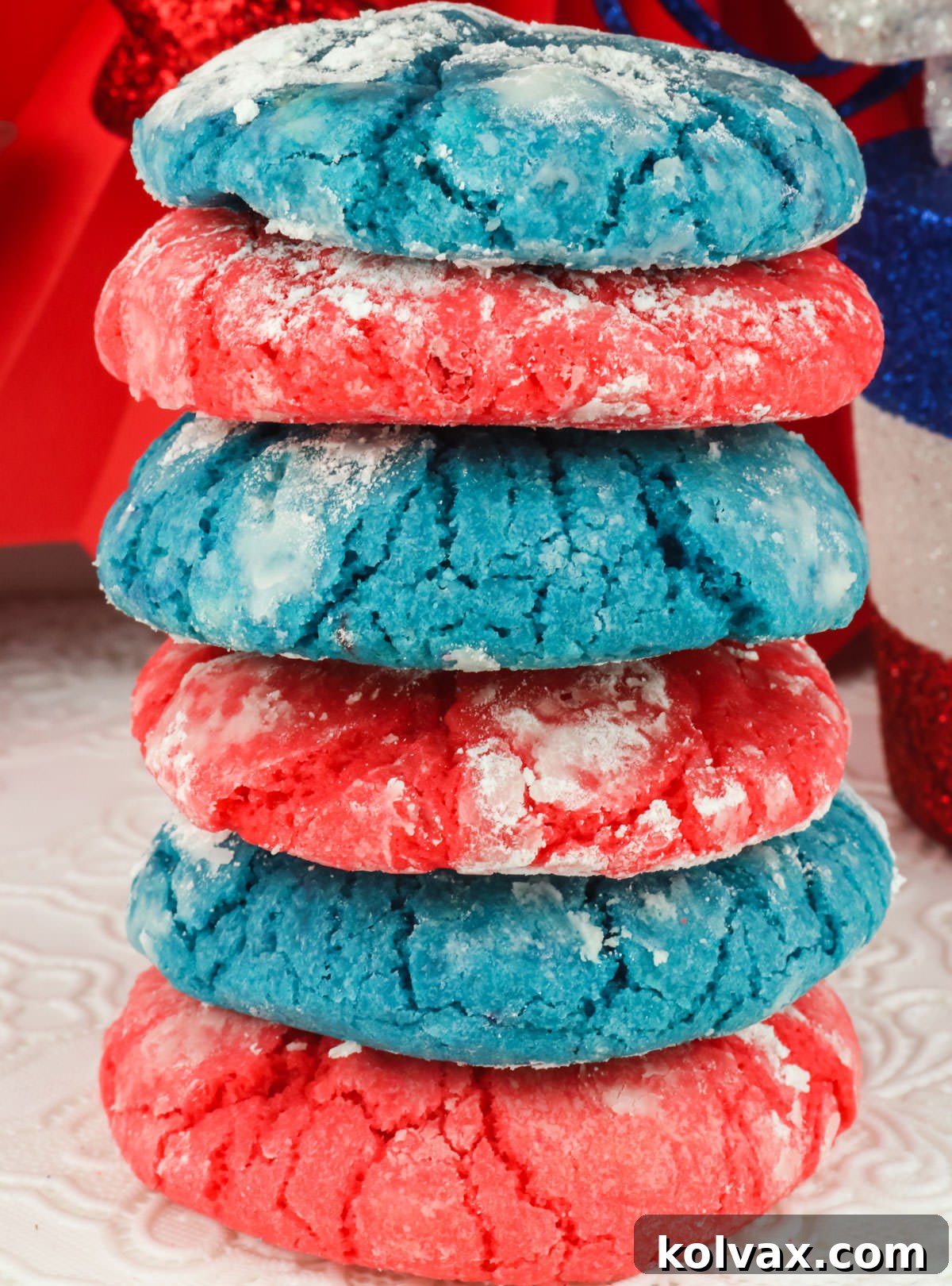 Closeup on a tall stack of vibrant Red White and Blue 4th of July Crinkle Cookies, dusted with powdered sugar, sitting on a white table.