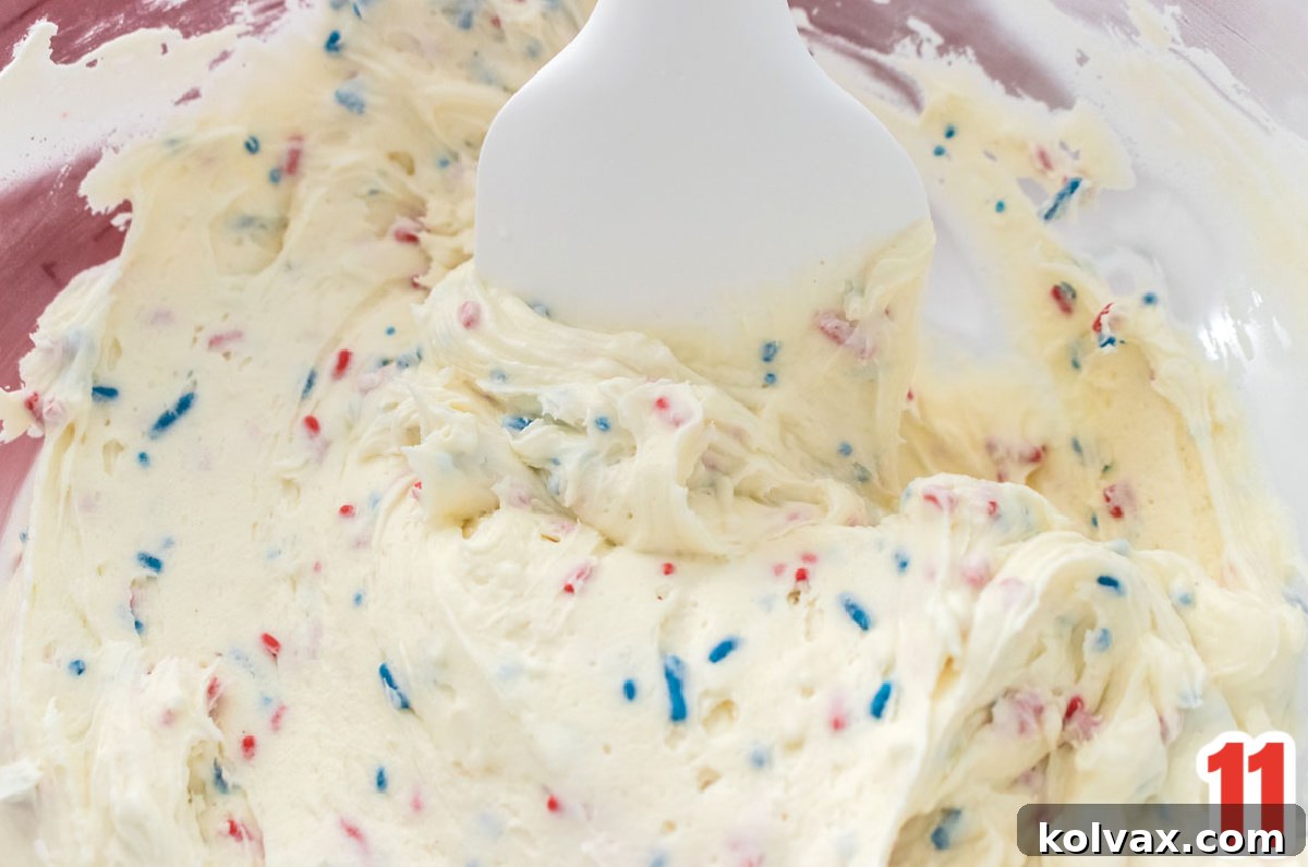 A close-up of a glass bowl filled with fluffy Homemade Ice Cream Frosting, with a white spatula resting inside, ready for tasting.