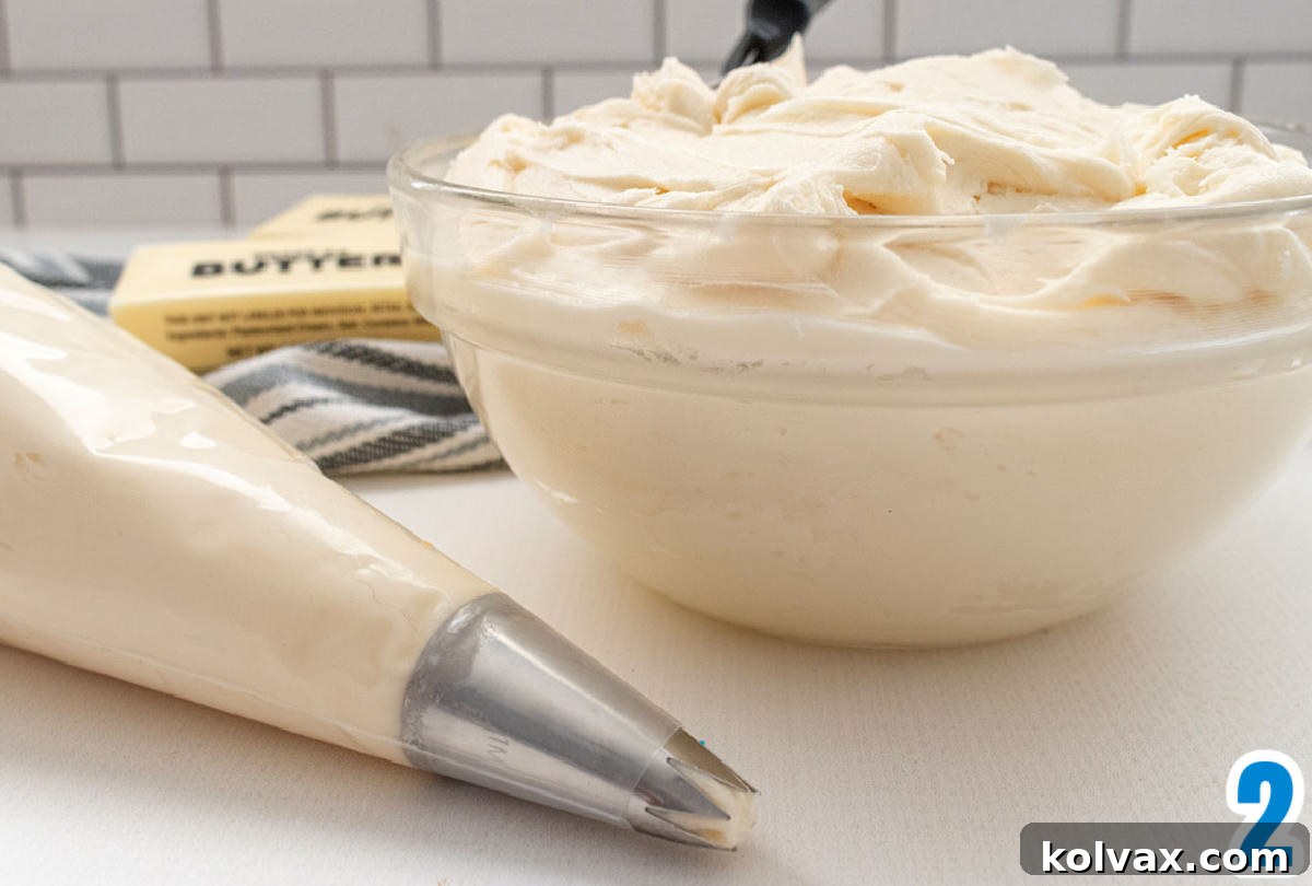 A clear mixing bowl brimming with fluffy, homemade buttercream frosting sits next to a piping bag neatly filled with the same creamy mixture, ready for cupcake decoration.