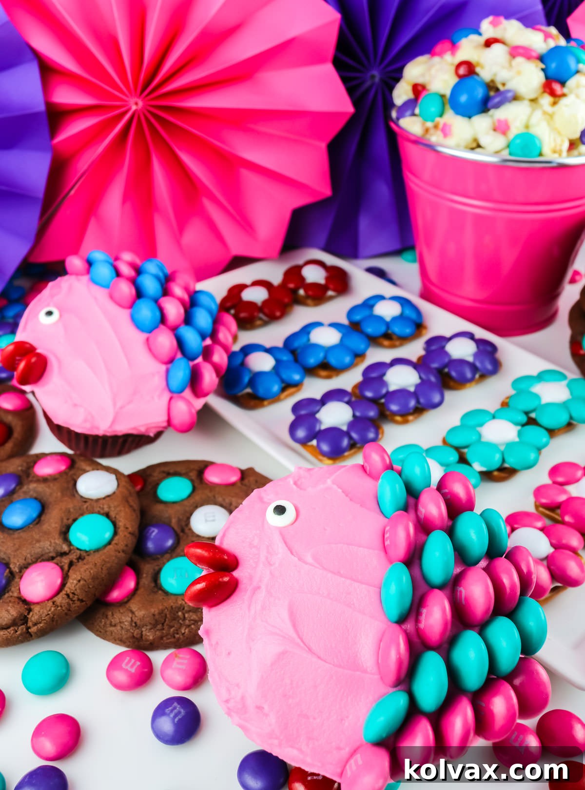 A series of desserts decorated with colored M&M including pretzel bites, popcorn, cupcakes and cookies.