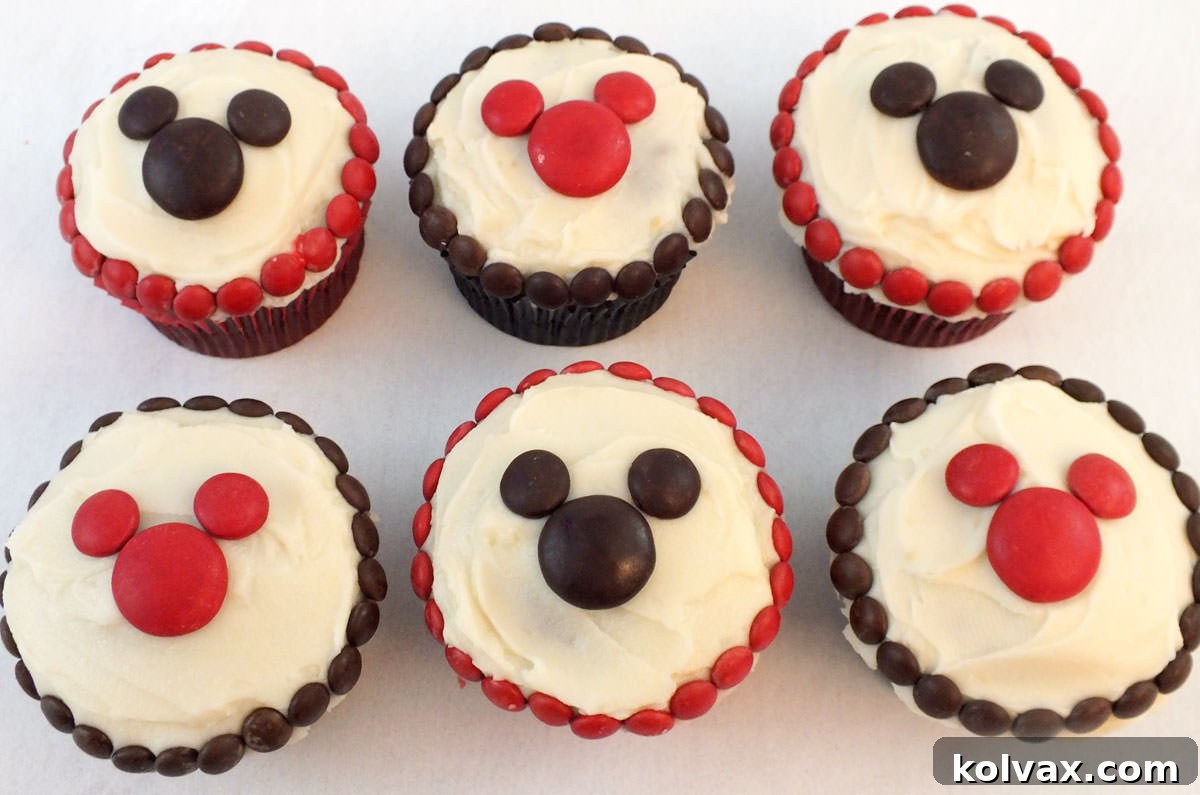 Six cupcakes decorated with M&M's sitting on a white table.