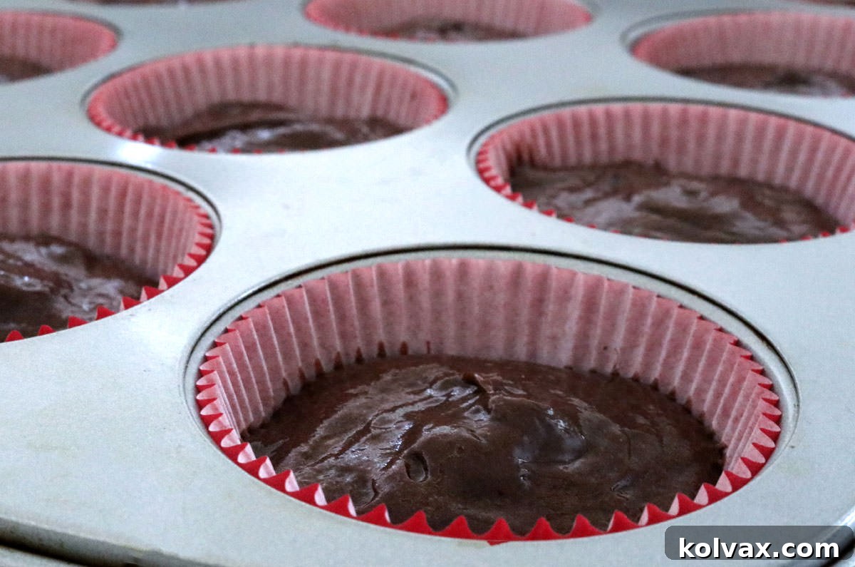 A cupcake pan filled with vibrant red paper liners, each containing smooth, dark chocolate cake batter, uniformly portioned and ready for baking.