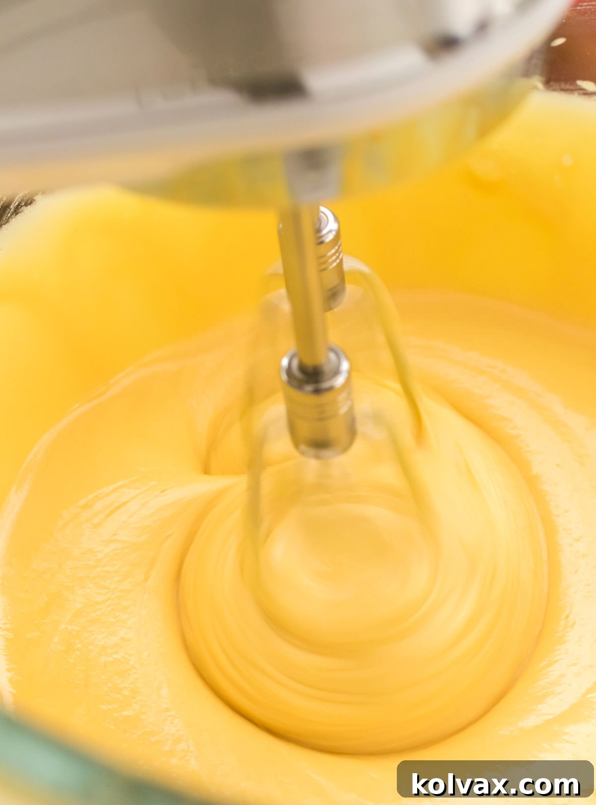 A clear mixing bowl filled with creamy, golden yellow cake batter, smooth and well-combined, reflecting the light.