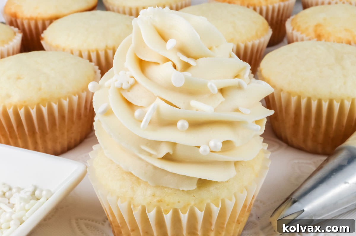 A delicious, perfectly frosted white cupcake with a swirled mound of homemade buttercream frosting, topped with sprinkles and presented in a pristine white liner.