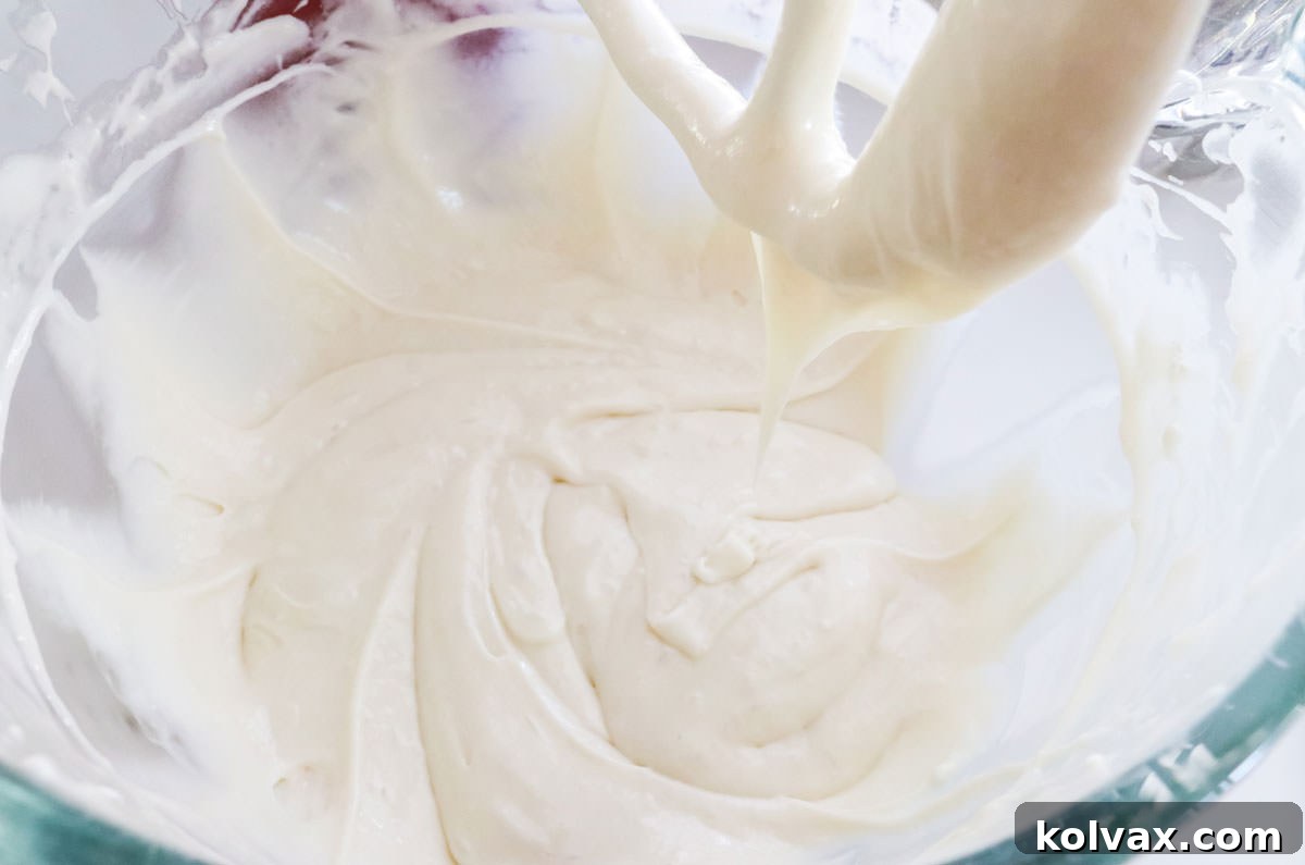 Closeup on a clear mixing bowl filled with pristine white cake batter, ready for baking. The batter is smooth and airy.