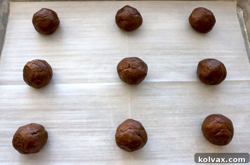 Perfectly rolled chocolate cookie dough balls, neatly spaced on a prepared baking sheet, eagerly awaiting their transformation in the oven.