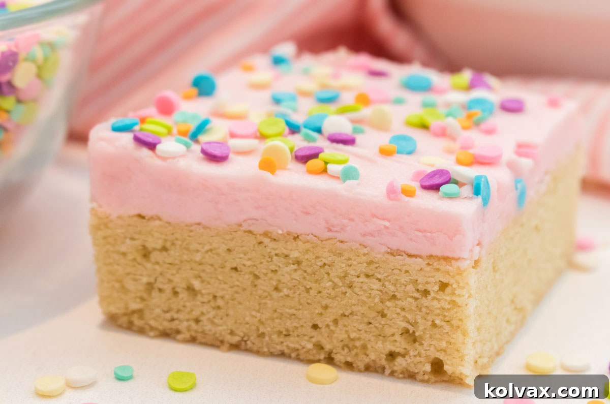 Closeup of a single The Best Sugar Cookie Bar, frosted with luscious pink homemade buttercream frosting and vibrant sprinkles, ready to be enjoyed.