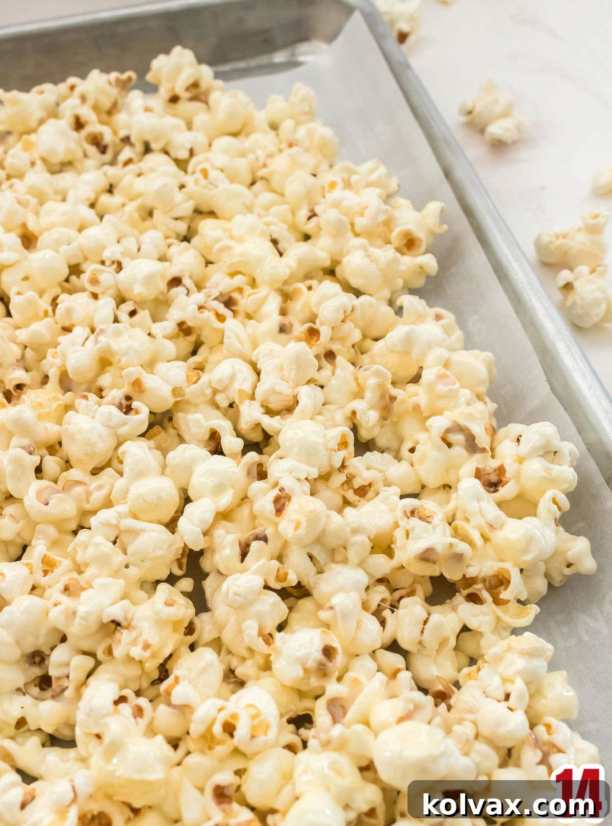 Marshmallow Popcorn cooling on a cookie sheet lined with parchment paper, spread out evenly.
