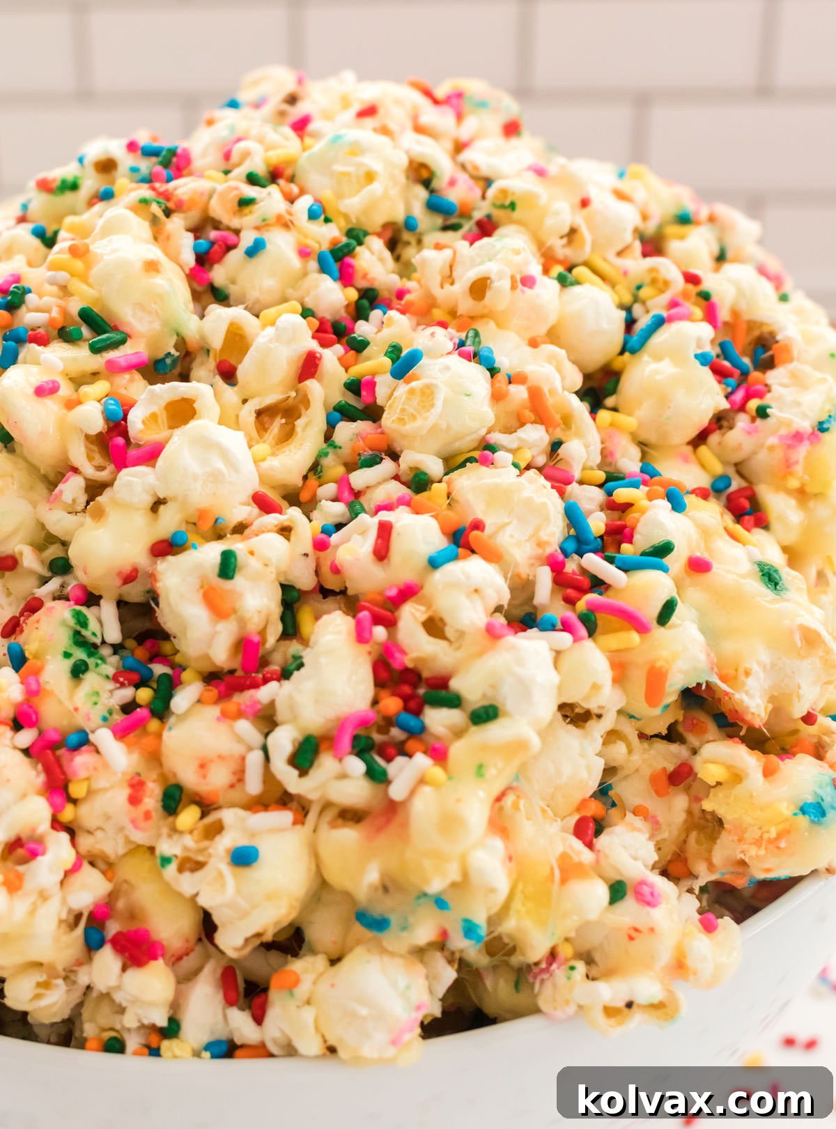 Closeup on a white serving bowl sitting on a pristine white table, generously filled with freshly made Cake Batter Popcorn, ready to be enjoyed.