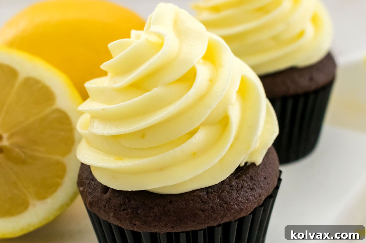 Closeup on two chocolate cupcakes frosted with The Best Lemon Cream Cheese Frosting sitting on a white serving platter next to a fresh lemon.