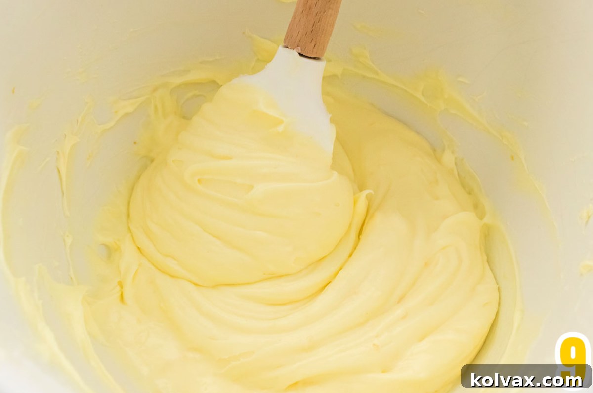 Lemon Cream Cheese Frosting in a white mixing bowl with a white wooden spatula.