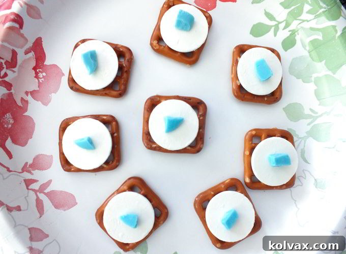 Pretzel Bites ready for the microwave - A batch of pretzel snaps topped with white and a tiny piece of blue candy melts, poised for melting in the microwave to create the base for delightful Frozen Snowflake Pretzel Bites.