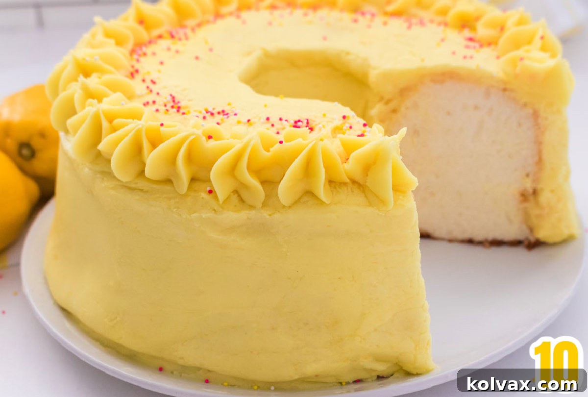 Closeup on an Angel Food Cake with Lemon Frosting sitting on a white table with a piece taken out of it and lemons off to the side.