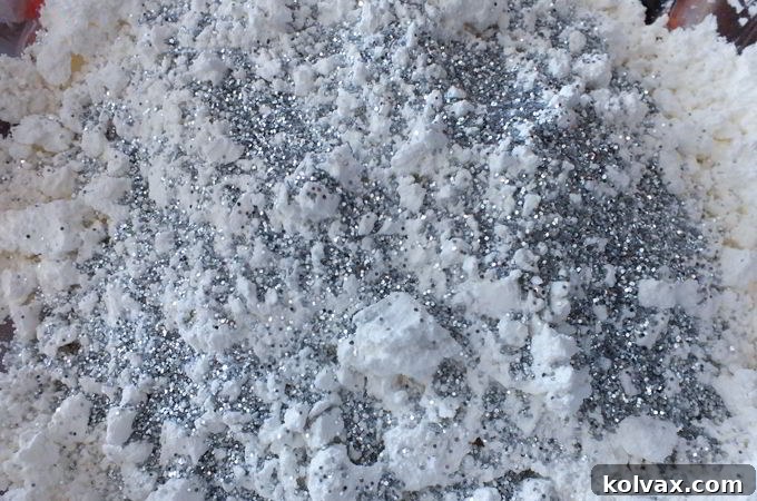 Sprinkling silver glitter onto the fully mixed DIY play snow, adding sparkle for a Frozen theme.