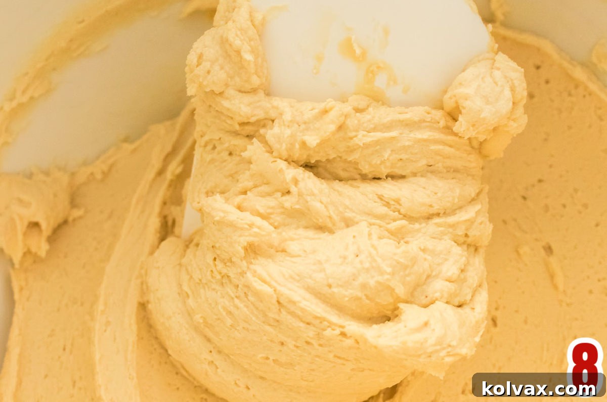 Closeup of a white mixing bowl filled with freshly made Gingerbread Frosting, with a white spatula resting inside.