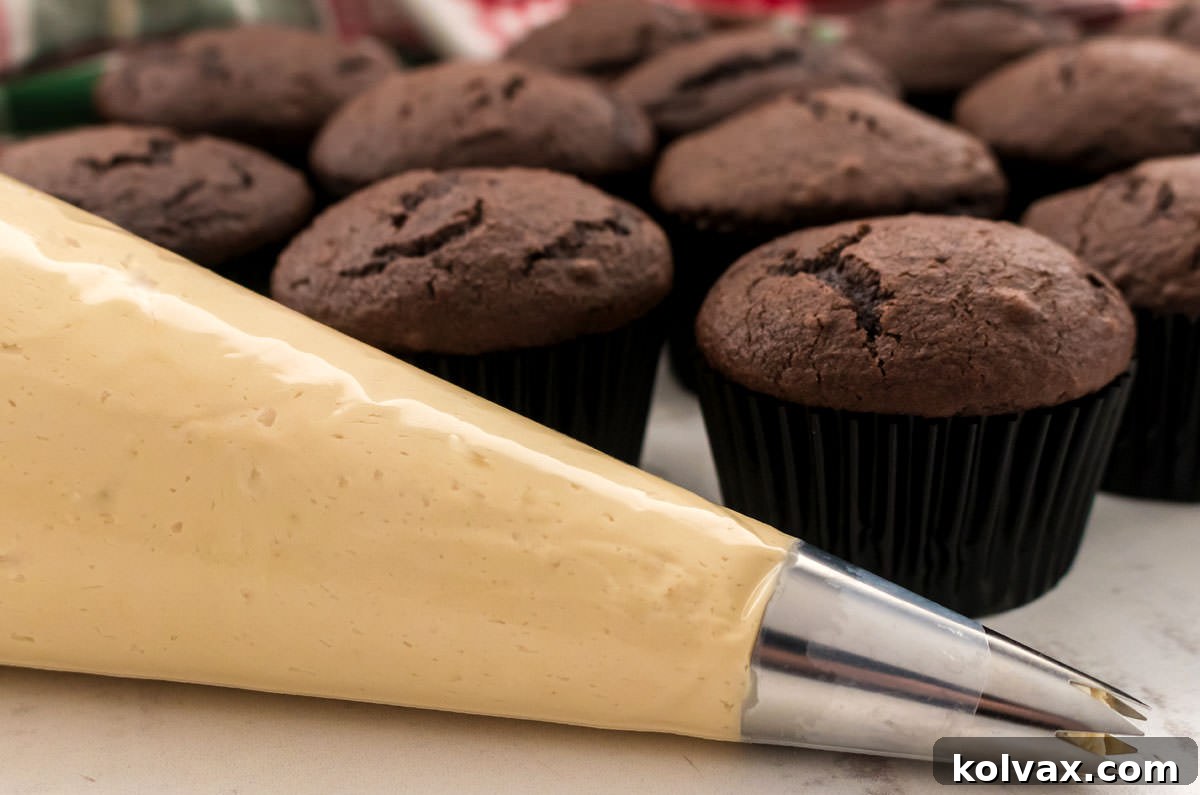 Closeup of a decorating bag filled with Gingerbread Frosting, positioned in front of a batch of unfrosted chocolate cupcakes.