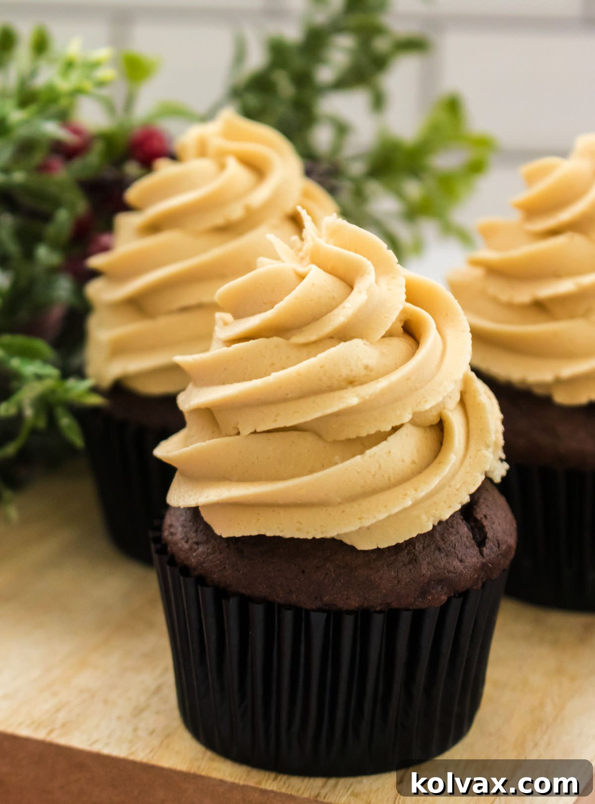 Closeup on three chocolate cupcakes topped with The Best Gingerbread Buttercream Frosting, beautifully arranged on a wooden cutting board.