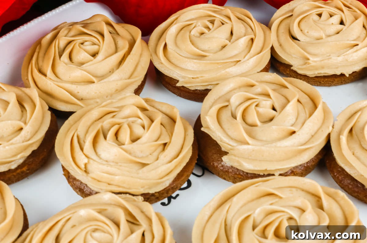 Closeup of a batch of Gingerbread Mini Cakes sitting on a white serving platter, beautifully decorated with creamy frosting swirls.