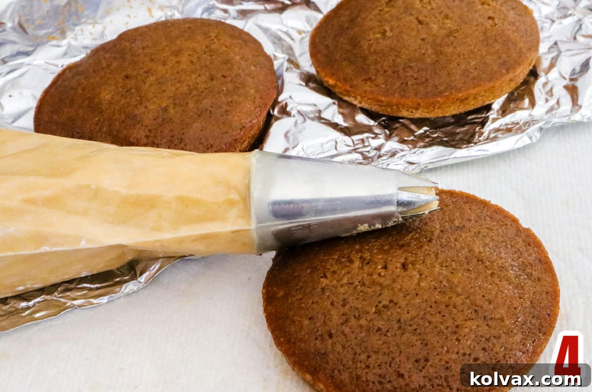 Three perfectly baked Gingerbread Mini Cakes sitting on a surface next to a piping bag filled with Gingerbread Buttercream Frosting, ready for decoration.