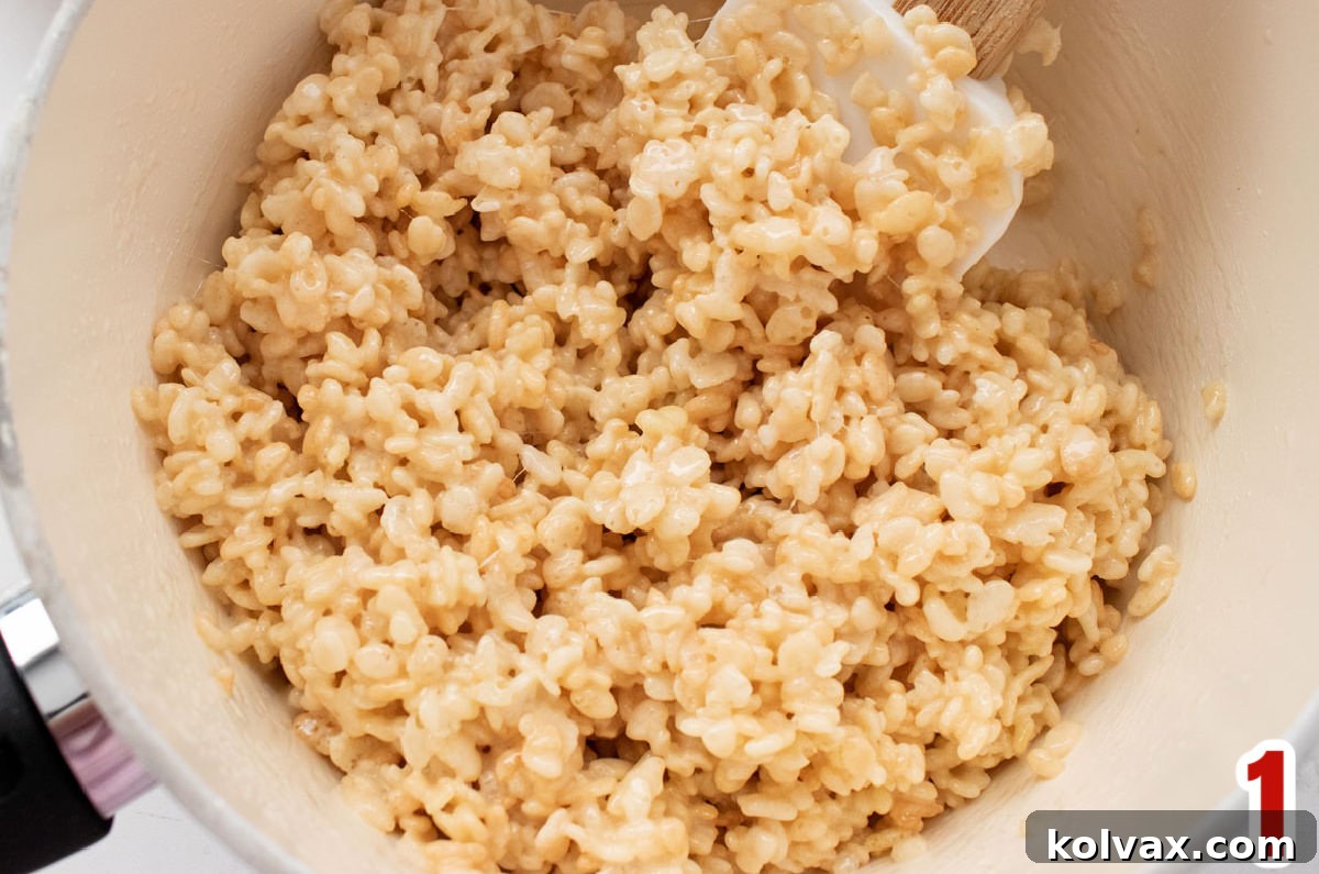 Closeup on a white sauce pan filled with warm Rice Krispie Treat mixture and a white wooden spoon.