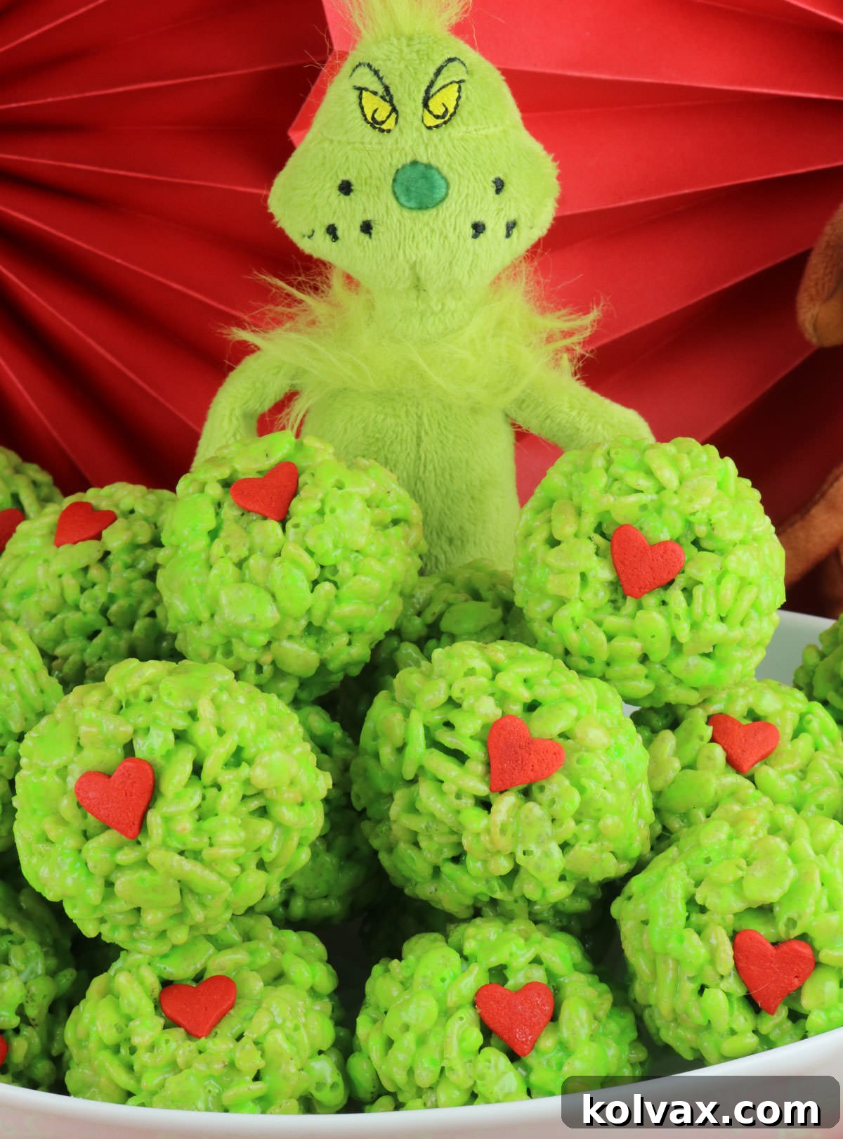 Closeup on a white serving bowl filled with Grinch Rice Krispie Treat Bites with a Grinch stuffed animal in the background.