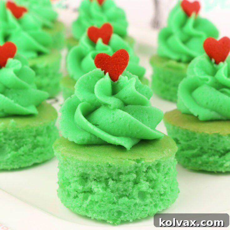 Grinch Cake Bites with green frosting and a red heart sprinkle on a white platter.
