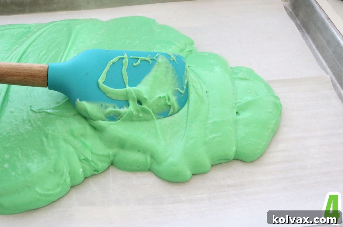 A close-up shot of vibrant green cake batter being carefully poured onto a parchment-lined baking sheet, preparing for an even bake.