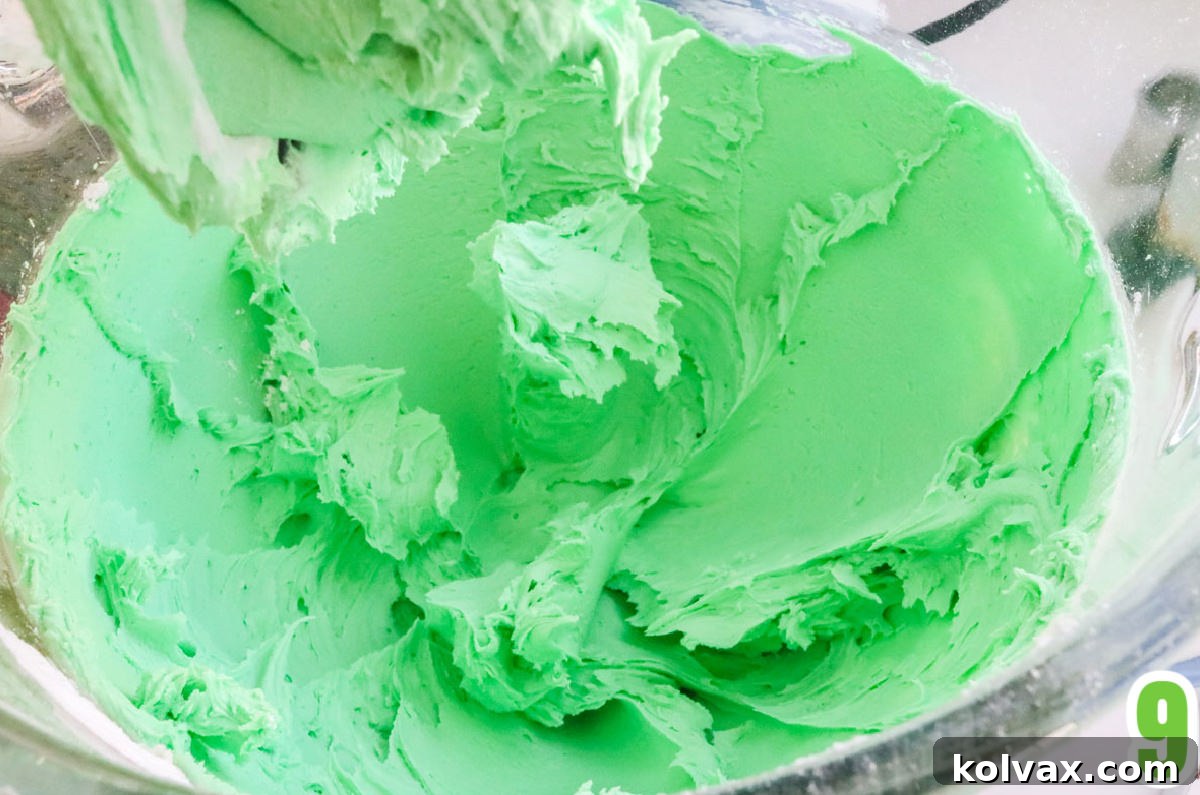 A glass bowl brimming with light green, fluffy buttercream frosting, perfectly tinted and ready to adorn the Grinch Cake Bites.