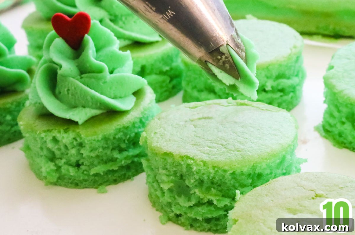 A decorating bag expertly piping a festive swirl of bright green buttercream onto a round green cake bite, ready for the finishing touch.