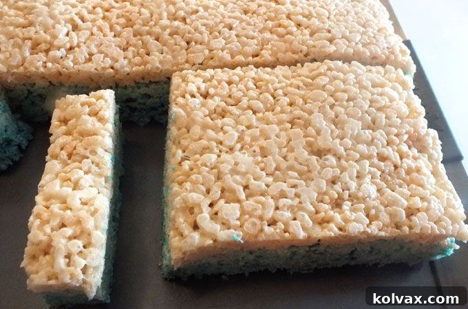 Slicing a 1-inch thick strip from one of the Ombre Rice Krispie Treat sections, revealing the beautiful gradient layers.