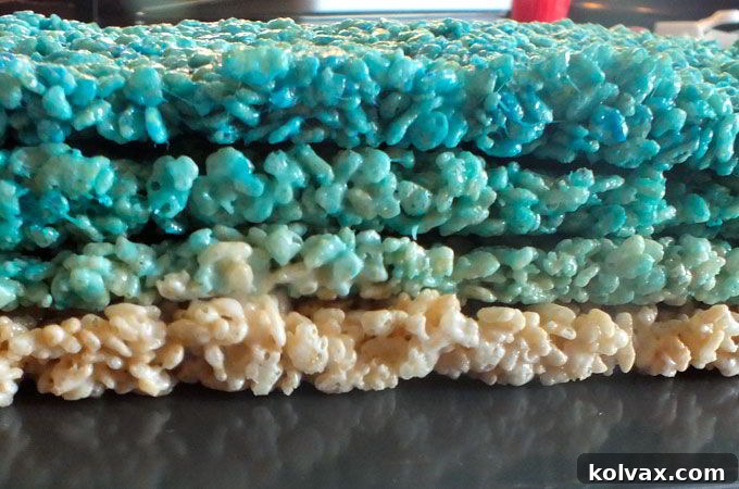 All four layers of Rice Krispie Treats, ranging from dark blue to white, are now stacked and ready for the final press and flip.