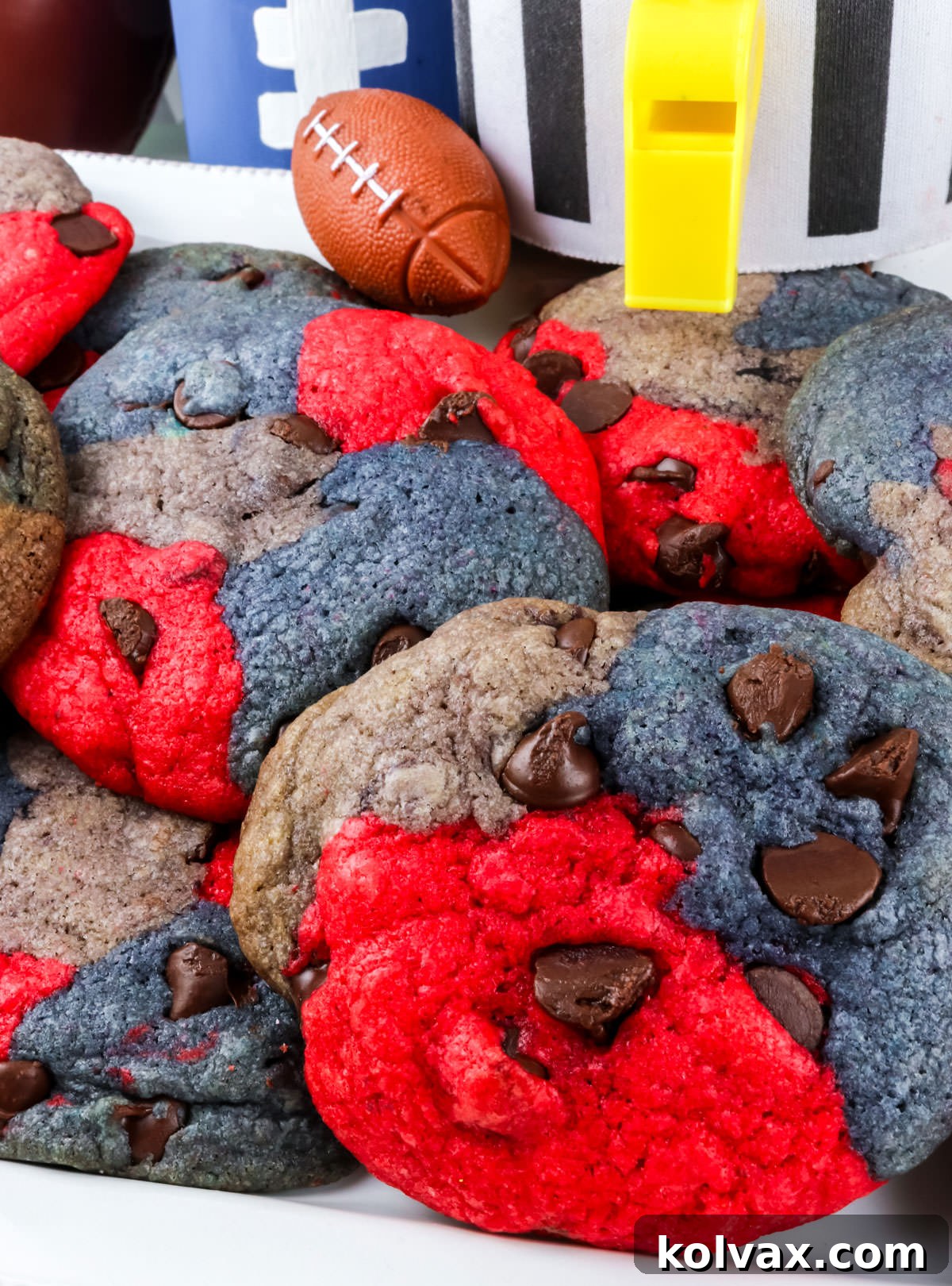 A close-up of a freshly baked batch of New England Patriots Chocolate Chip Cookies, artfully arranged on a white dessert platter alongside festive football decorations.