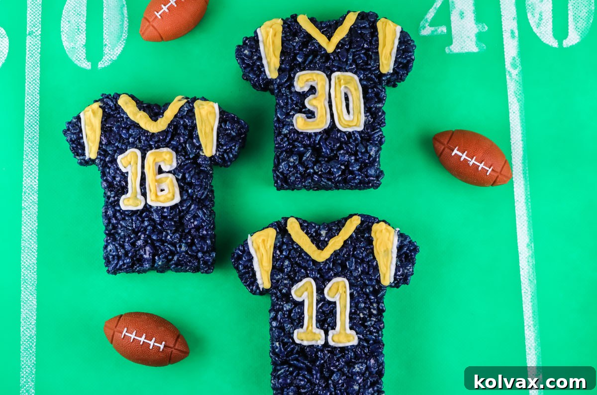 Three Los Angeles Rams Rice Krispie Treats laying on a football field tablecloth and mini footballs, showcasing vibrant team colors.