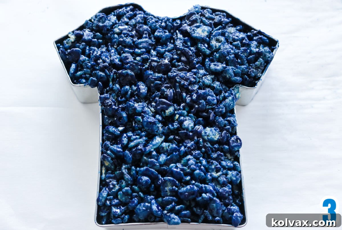 Closeup on a T-Shirt shaped cookie cutter filled with blue Rice Krispie Treat mixture, ready to be molded.