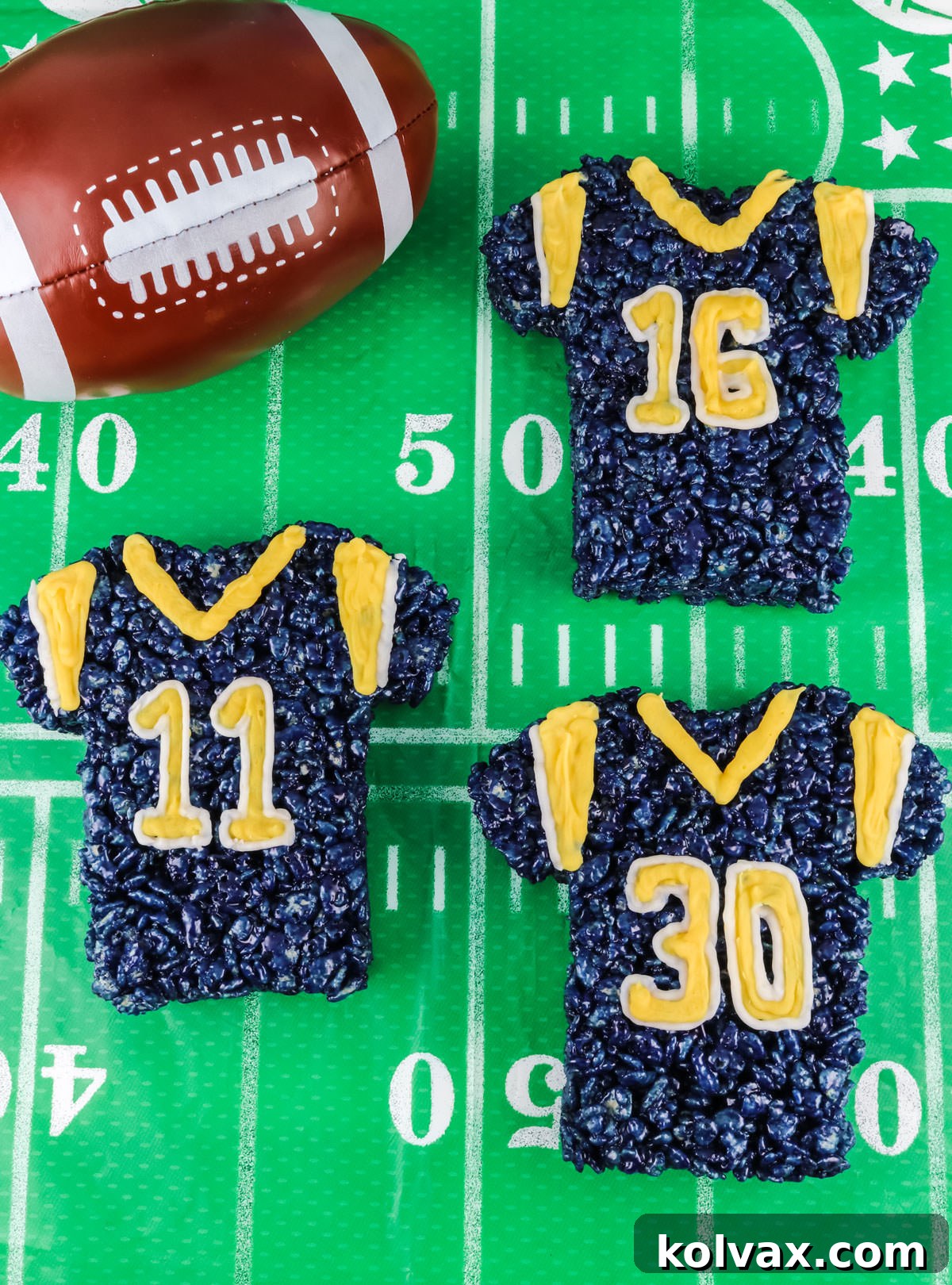 Three decorated Los Angeles Rams Rice Krispie Treats laying on a Football field table cloth, ready for celebration.