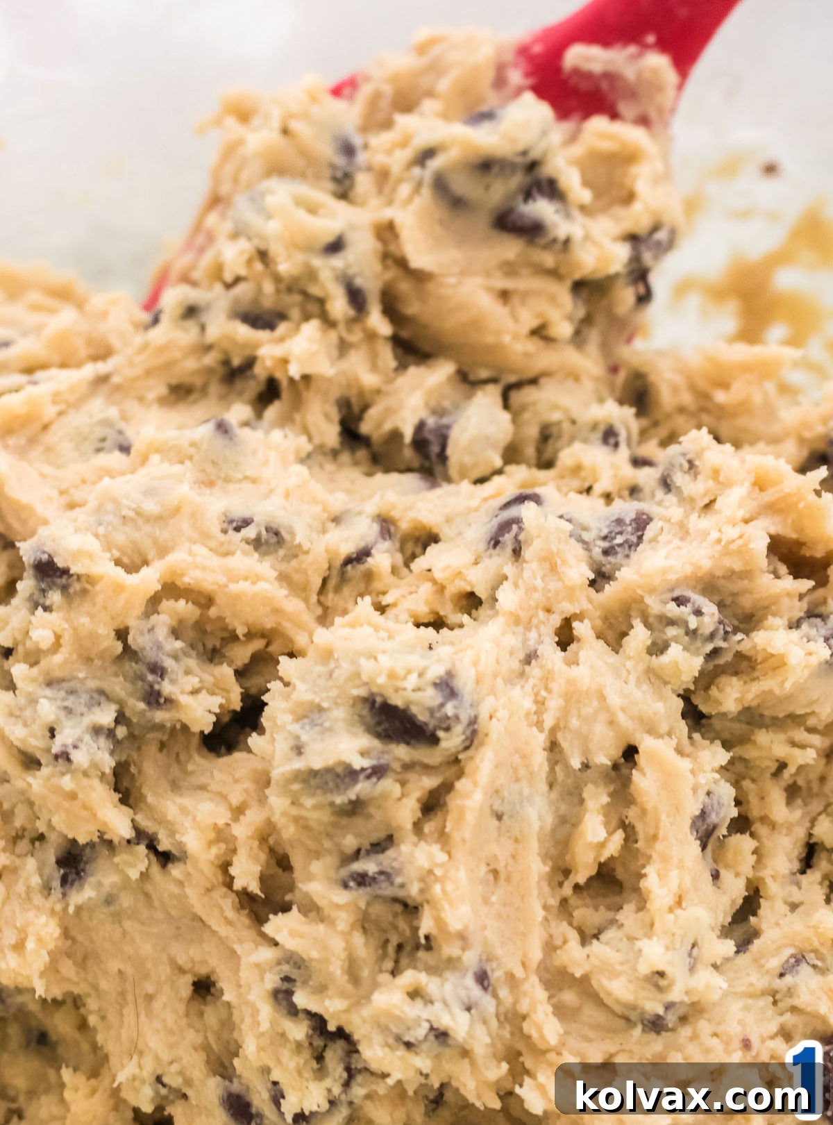 Closeup on a white mixing bowl filled with chocolate chip cookie dough and a red spoon.