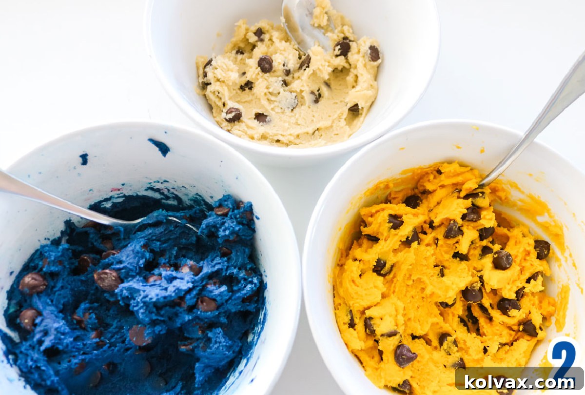 Closeup on three white bowls filled with regular colored Chocolate Chip Cookie dough and dough tinted blue and yellow.