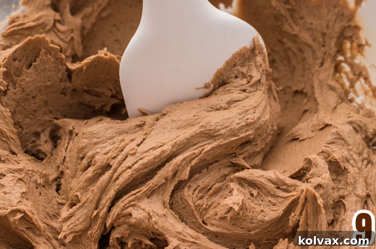 Closeup on a glass mixing bowl filled with Mocha Icing and a white spatula.