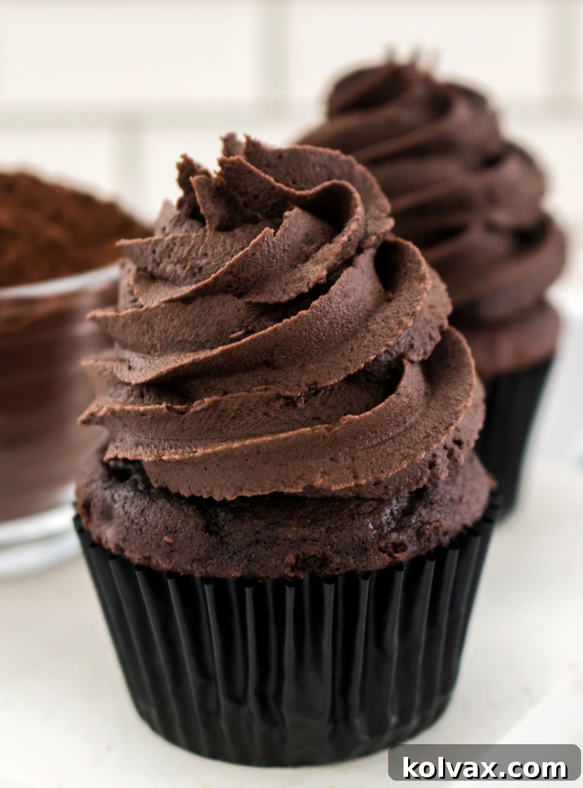 A single chocolate cupcake lavishly topped with the best dark chocolate buttercream, sitting elegantly beside a bowl of cocoa powder.