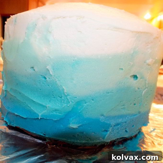 Demonstration of smoothing colored buttercream frosting on the side of a cake with a graduated spreader to create a beautiful ombre design.