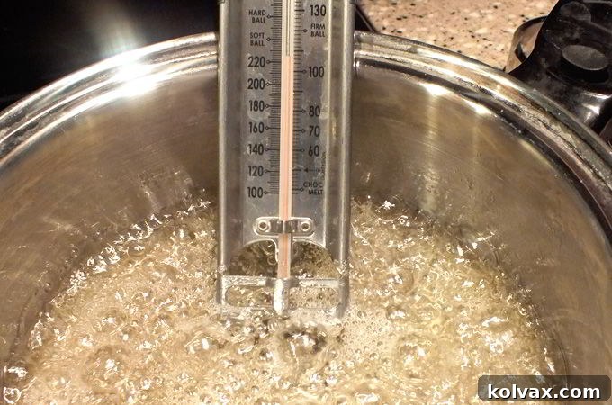 Candy mixture for ice castle topper brought to a rolling boil in a saucepan, with a candy thermometer inserted to monitor temperature.