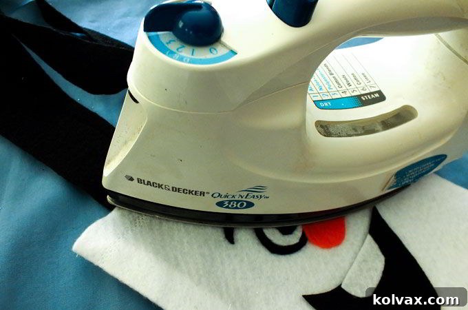 Using a hot iron to carefully affix iron-on letters to the felt party favor bags, ensuring a lasting personalized finish.